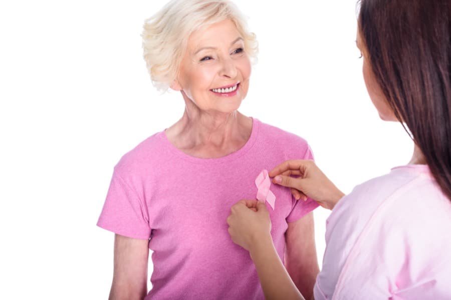 Mujer mayor sonriendo mientras otra persona le coloca un lazo en la camiseta