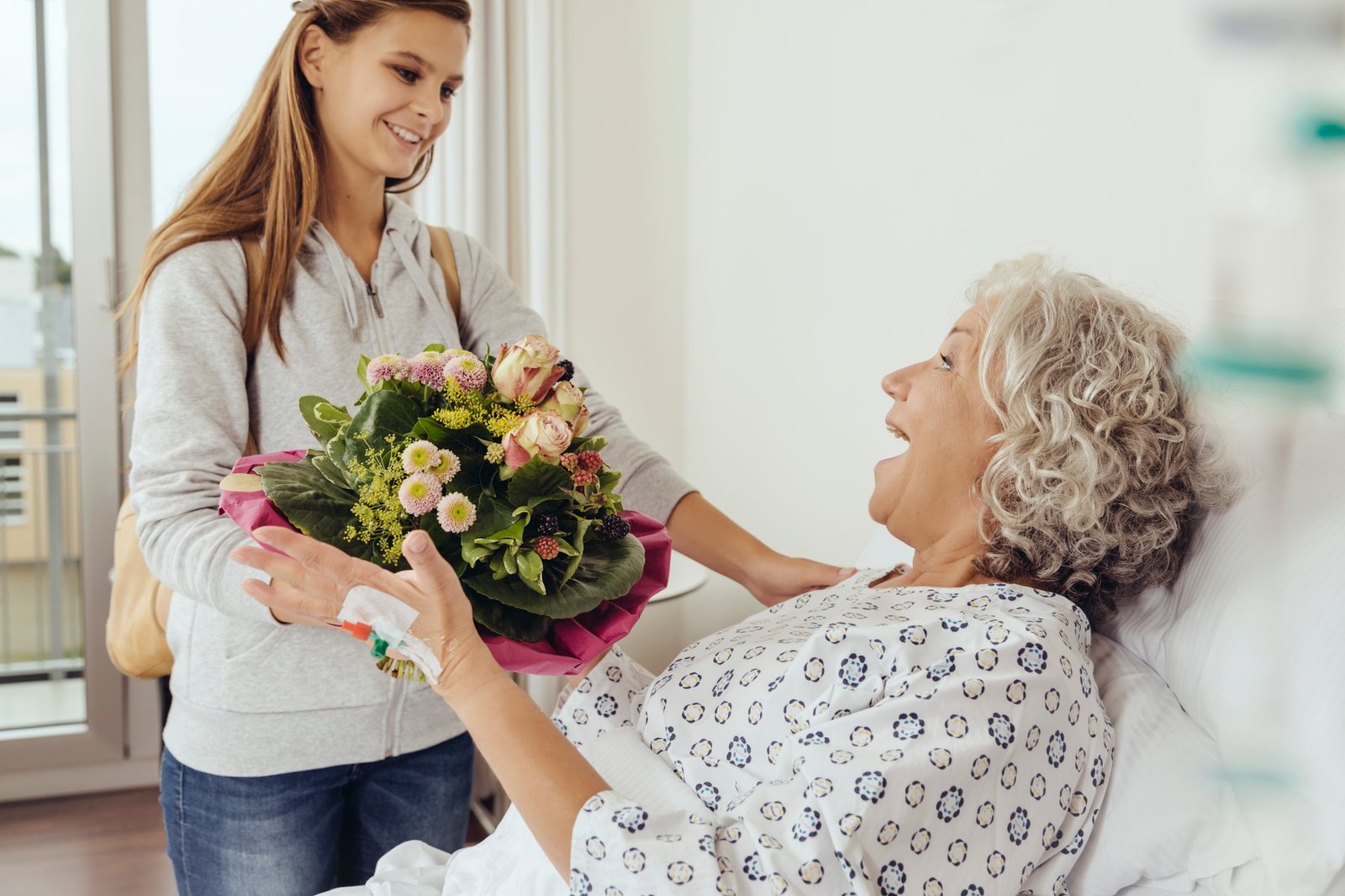 acompañamiento en hospital o residencias 2 Granddaughter visiting grandmother in hospital, bringing bunch of flowers
