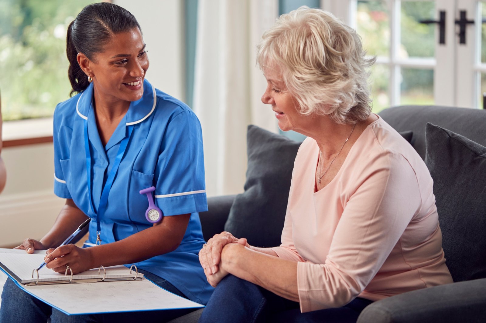 Quiénes somos 1 Senior Woman At Home Talking To Female Nurse Or Care Worker In Uniform Making Notes In Folder